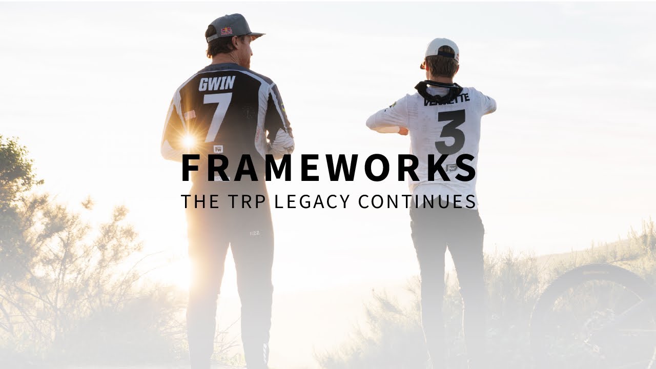Two people wearing branded clothing with 'Frameworks' and 'TRP' text, standing in a desert landscape.