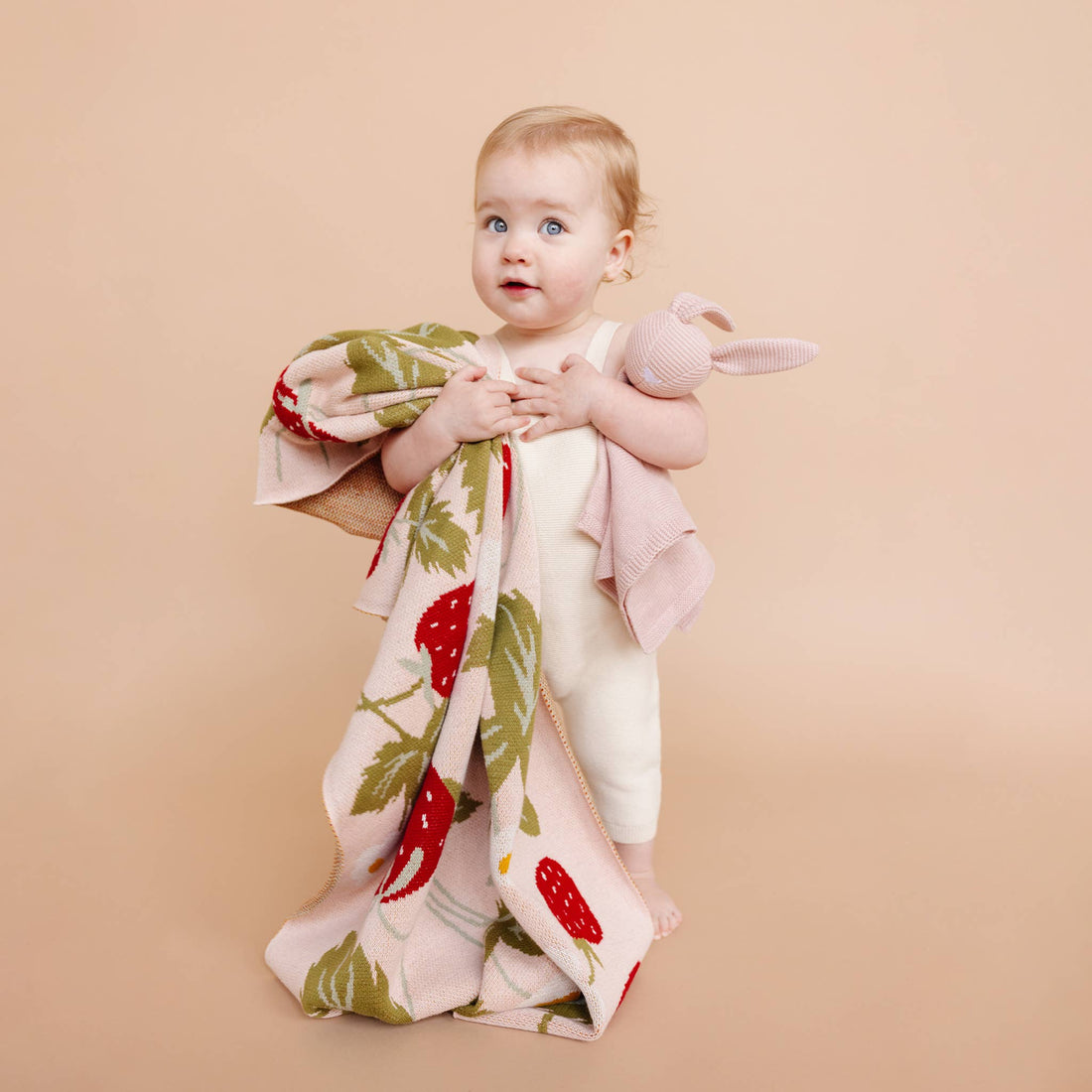 Baby holding The Blueberry Hill Strawberry Bunny organic baby blanket
